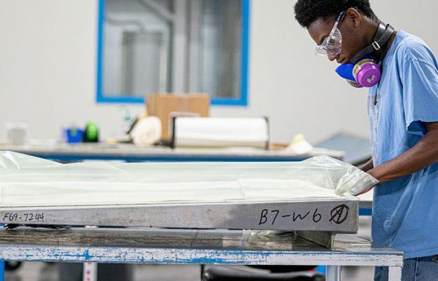 Man wrapping large metal part in plastic at a table