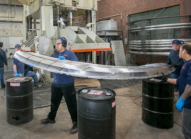 People lifting large sheet metal form over barrels