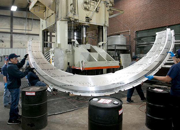 Two men lifting large metal part over barrels