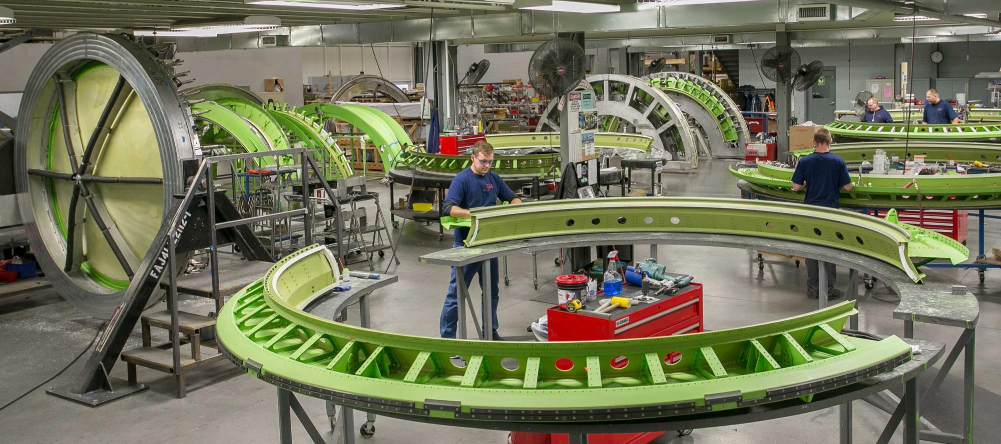 Wide shot of factory with men working on bulkhead assembly